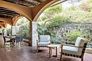 Patio esterno con parete in pietra, tavolo di legno e due sedie.