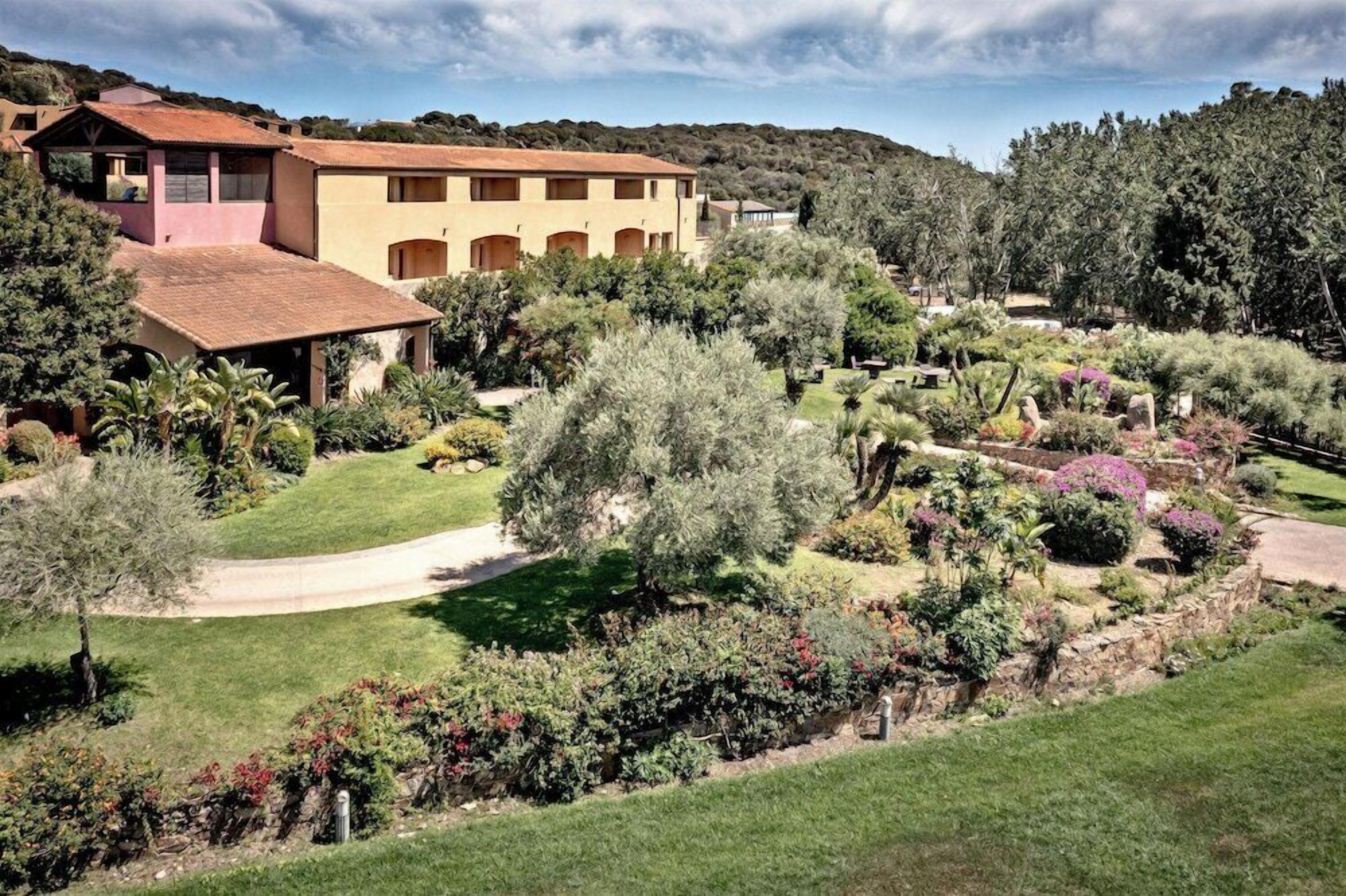 Un edificio imponente con numerosi balconi, circondato da un giardino curato e ricco di piante, sotto un cielo sereno.