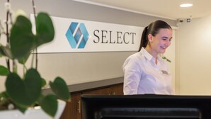A reception area with a sign that reads 'SELECT' and a receptionist standing behind a desk. - Select Hotel Mainz (Mainz)