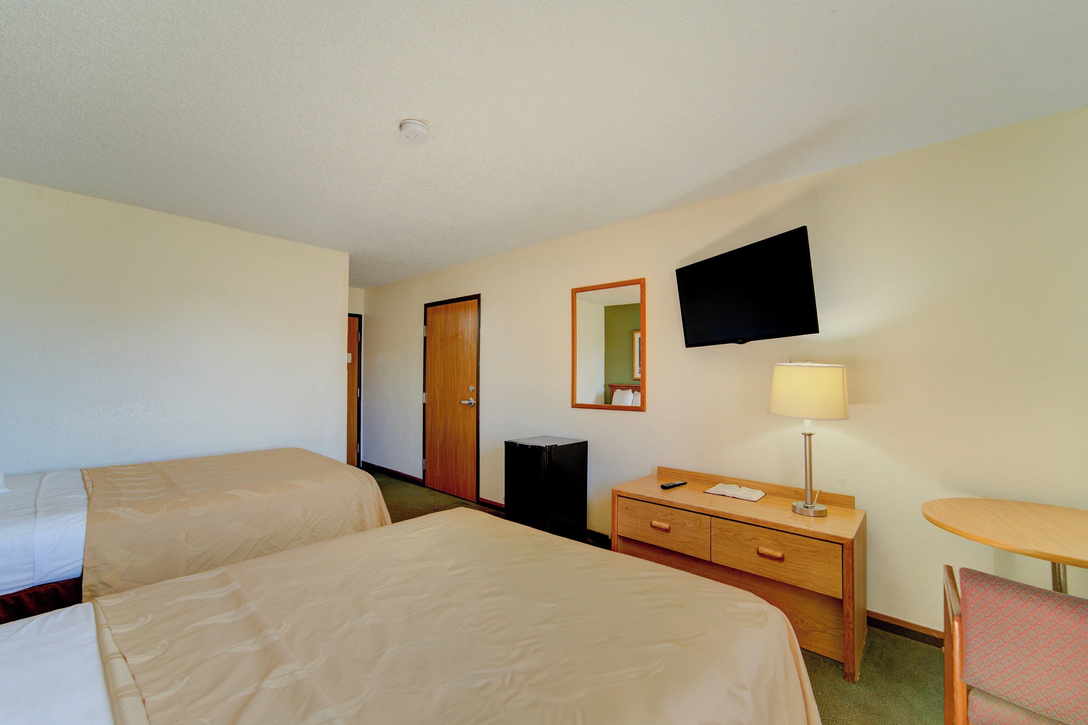 Une chambre d’hôtel avec deux lits, un bureau avec une lampe, une chaise, une télévision et un miroir.