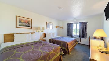 A hotel room with two beds, a desk with a lamp, a television, and a window with curtains.