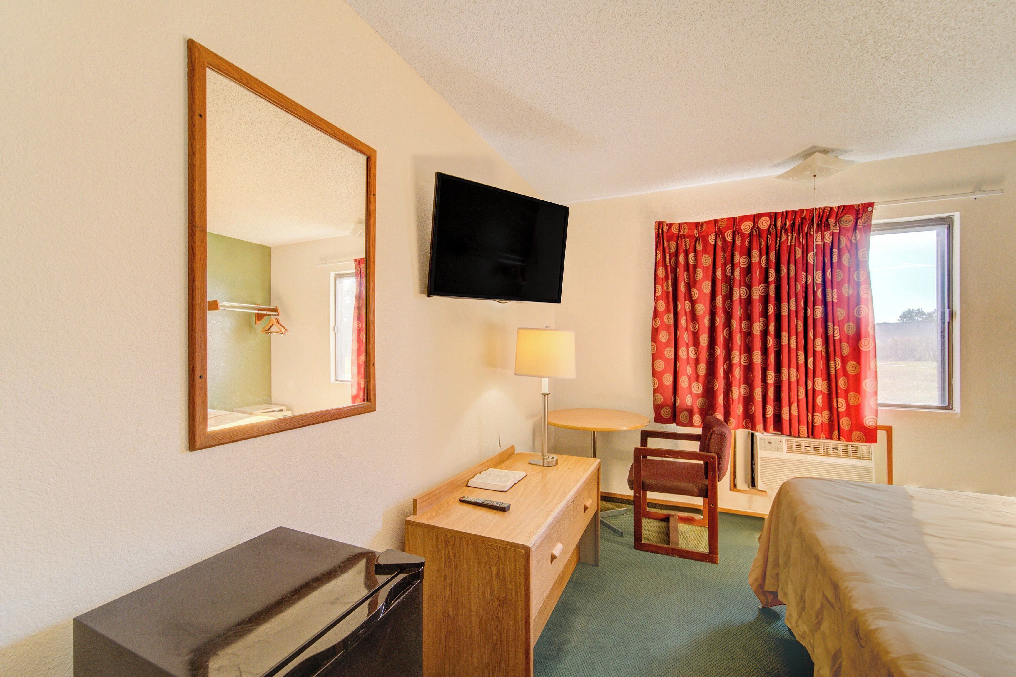 Ein Hotelzimmer mit Bett, Schreibtisch, Stuhl, Fernseher und einem Fenster mit Vorhängen.