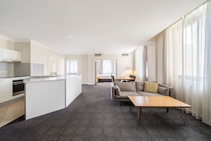 Una habitación de hotel moderna con kitchenette, comedor, sofá y ventanas amplias.