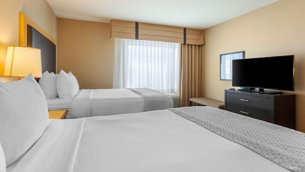A hotel room with two beds, a TV, a desk, and a window with curtains. - Cambria Hotel Ft Collins (Fort Collins)