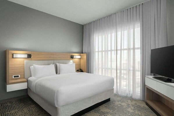 Quarto de hotel com cama grande, televisão, mesa de cabeceira e janela com cortinas.
