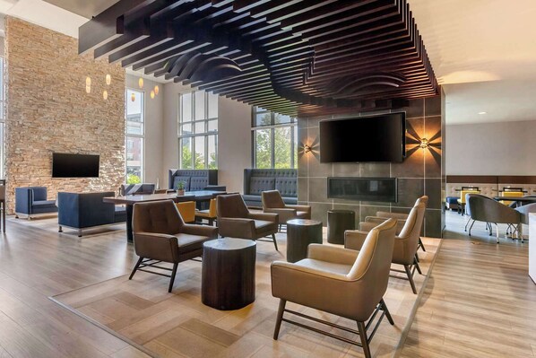 A modern lounge area with sofas, chairs, a fireplace, and a flat-screen TV. - Cambria Hotel Ft Collins (Fort Collins)