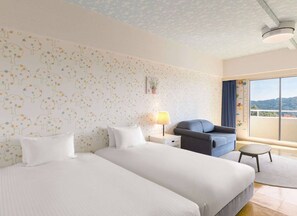 Habitación de hotel con dos camas, un escritorio, una silla y un ventanal con vistas.
