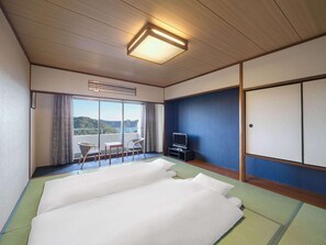 Een hotelkamer met tatami matten, een bed, een televisie, een balkon met uitzicht en een schuifdeur.