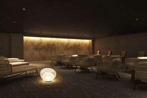 Een kamer in gedempt licht met een behang met patroon, verschillende rieten stoelen en een bijzondere bolvormige lamp.