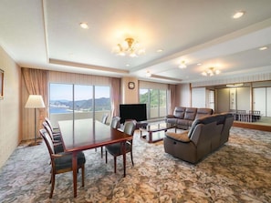 A hotel room with a dining table, chairs, a sofa, a TV, and a large window offering a scenic view. - Grand Mercure Awaji Island Resort & Spa (Minamiawaji)