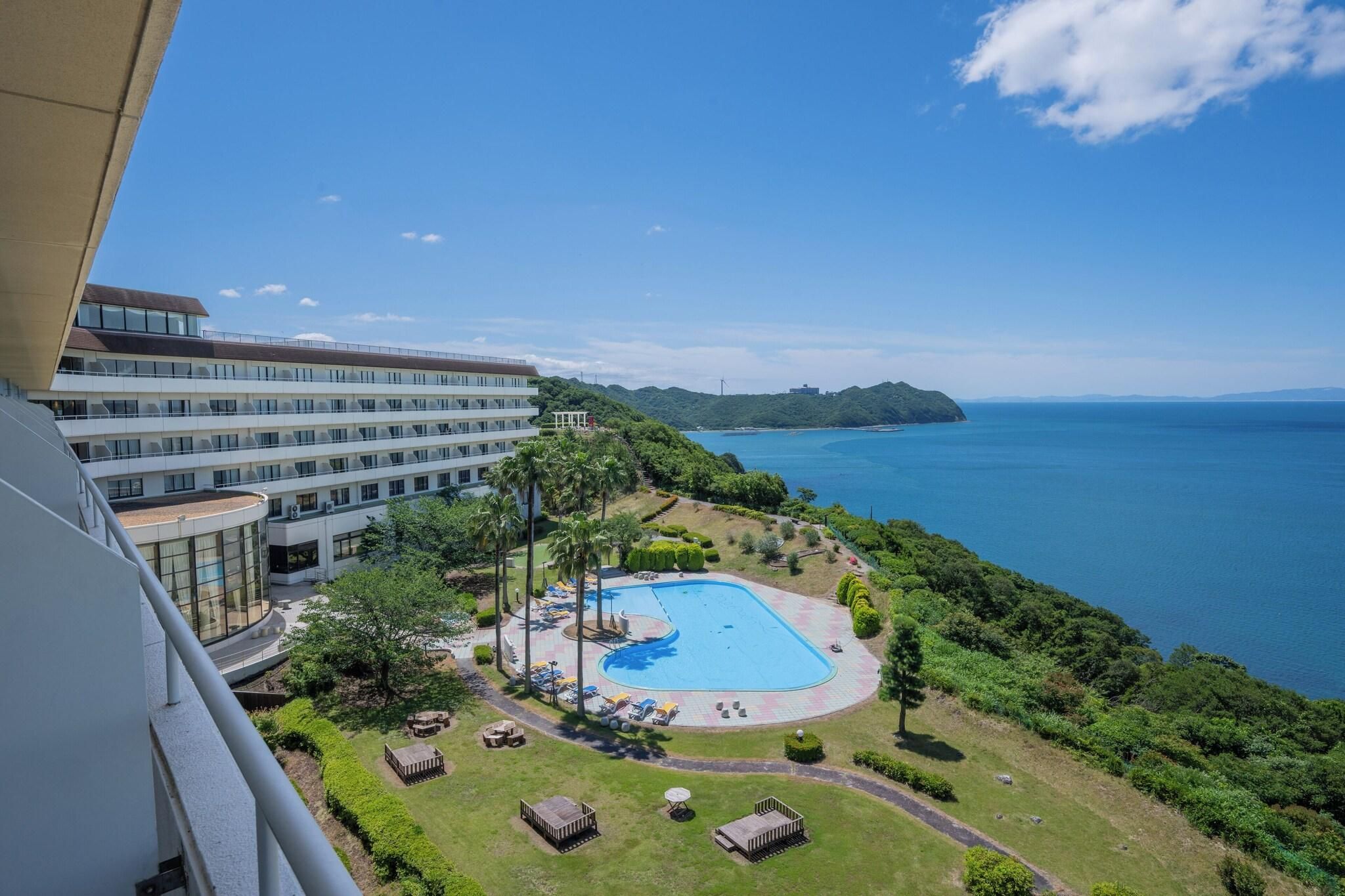 Un hotel con piscina rodeado de vegetación y vistas al mar.