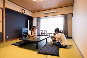 Una habitación con suelo de tatami, un televisor, un reloj y una ventana con cortinas.