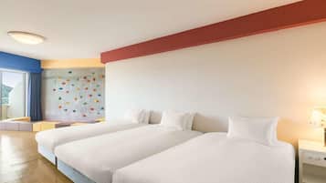 Una habitación de hotel con dos camas, una pared de escalar, un ventanal con cortinas y una mesita de noche con lámpara.