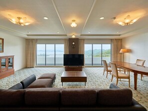 A hotel room with a large flat-screen TV, a sofa, a dining table with chairs, and a view of the sea. - Grand Mercure Awaji Island Resort & Spa (Minamiawaji)