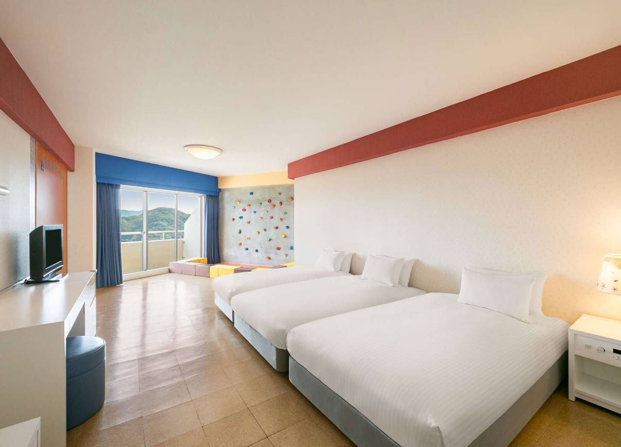 Habitación de hotel con dos camas, un escritorio, televisión y vista al exterior.