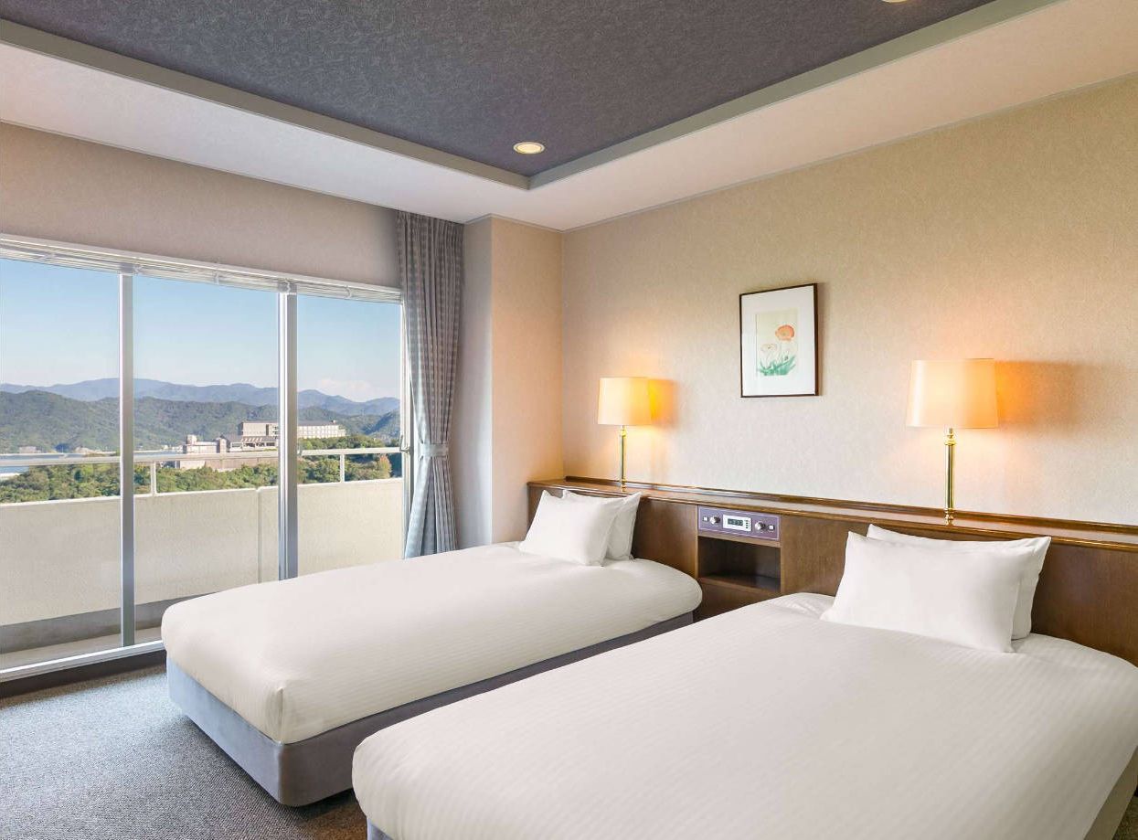 Habitación de hotel con dos camas, un ventanal con vistas y una mesita de noche con lámparas.