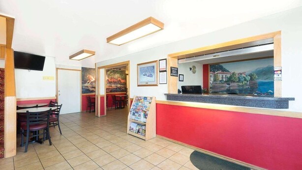 A reception area with a counter, chairs, a television, framed pictures, and a view of a coastal scene. - Super 8 Sheridan (Sheridan)
