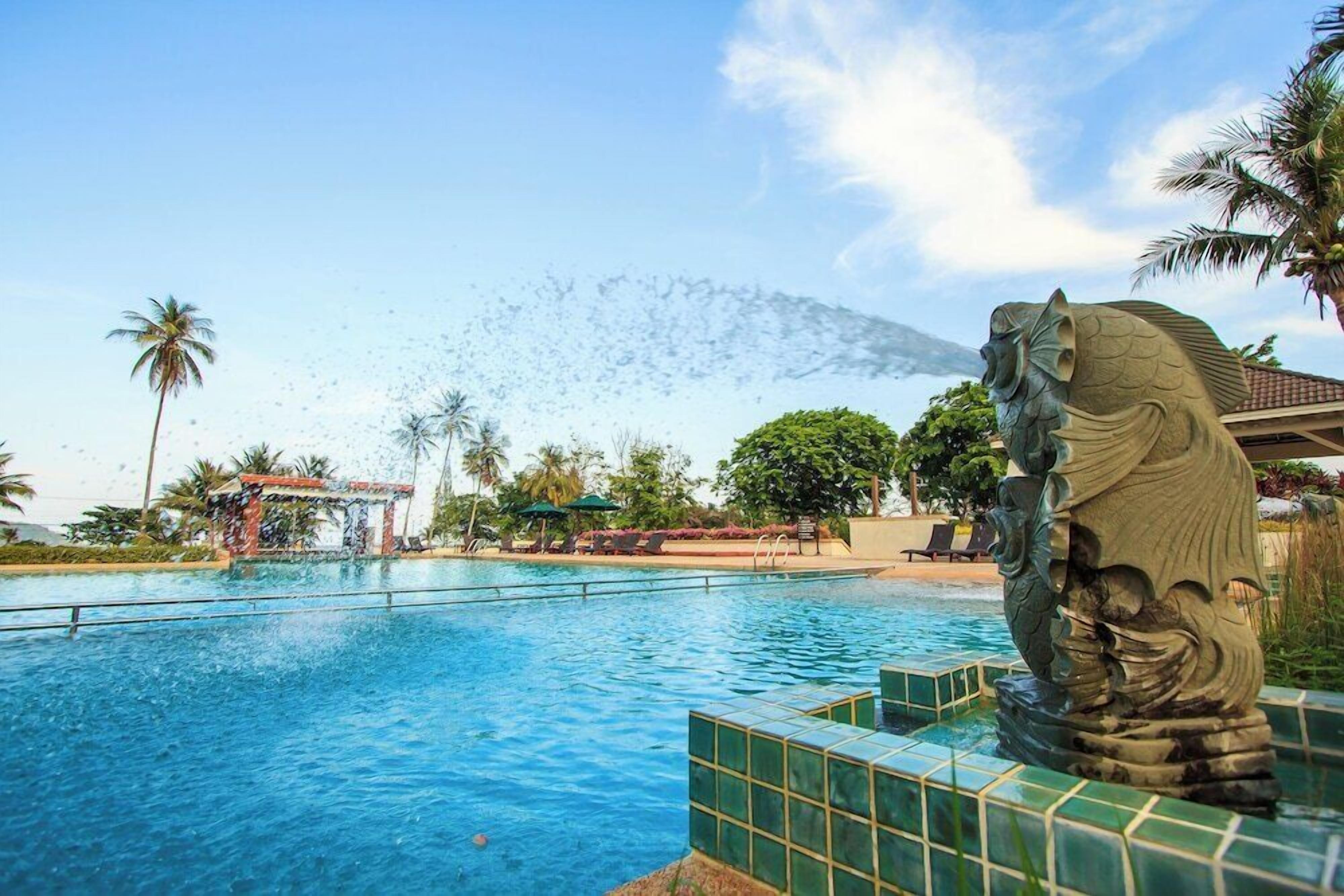 A swimming pool with a decorative stone lion statue, palm trees, and a clear sky.