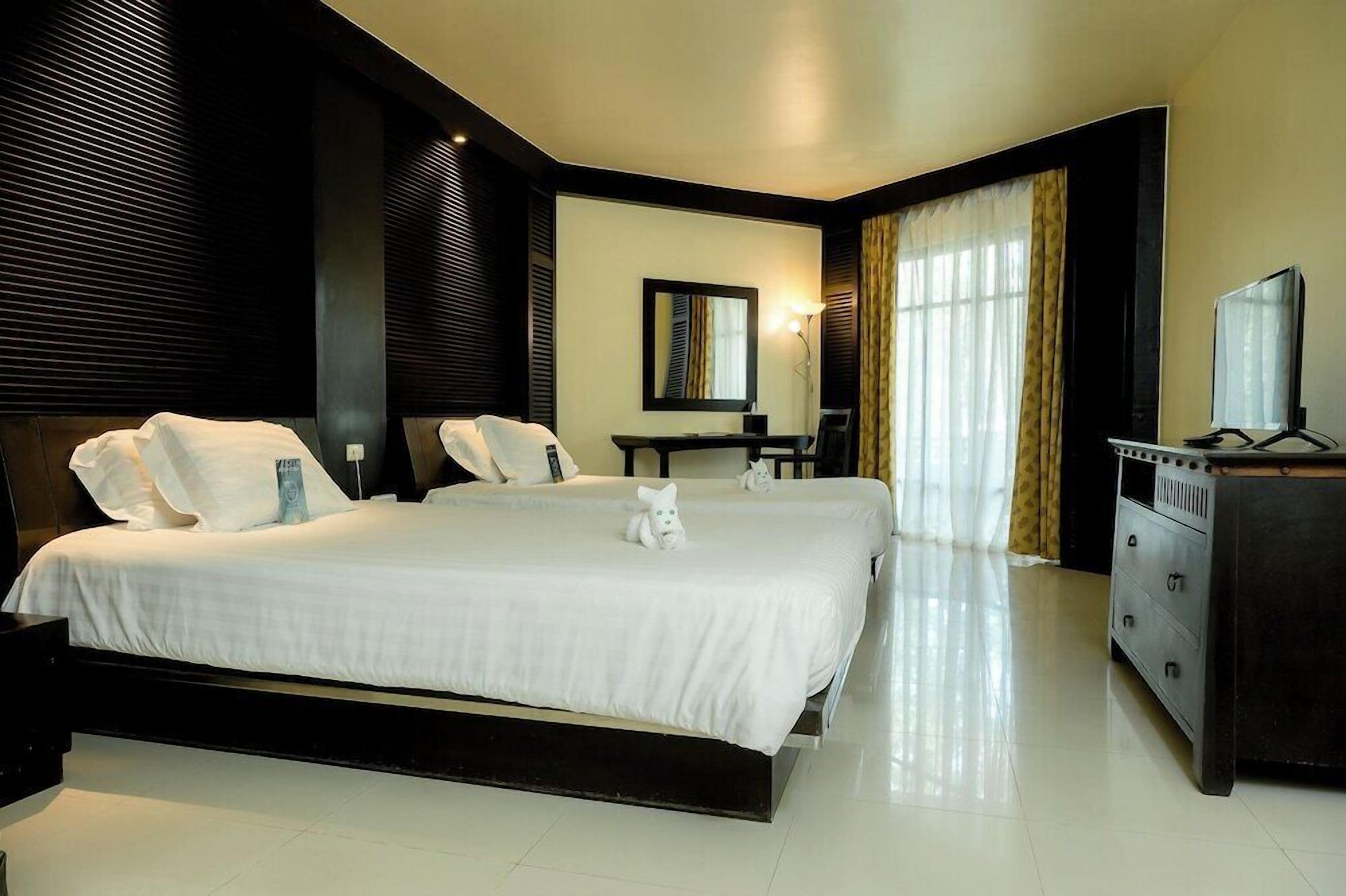 A hotel room with a large bed, a desk, a chair, a dresser, and a television.