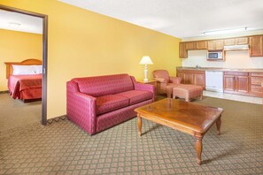 Una habitación de hotel con sofá, una mesa de centro de madera, una lámpara, una silla, una cama y una kitchenette.