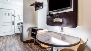 A hotel room with a round table, a TV mounted on the wall, and a door with a sign.