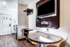 Une chambre d’hôtel avec une table ronde, un téléviseur fixé au mur, une porte avec une pancarte et une petite étagère.
