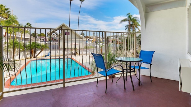 A balcony with a pool, blue chairs, and a table.