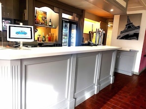 A bar area with a computer monitor, bottles, and a painting of the Eiffel Tower.