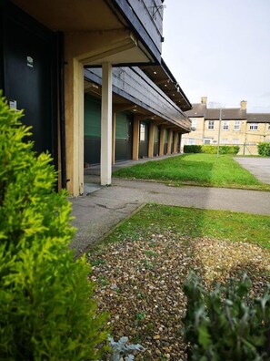 A building with a covered walkway, a grassy area, and a gravel path.