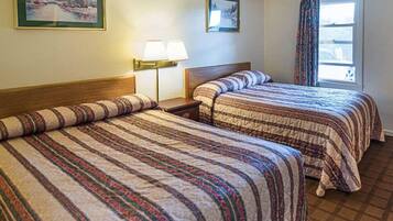 A hotel room with two beds, a nightstand, a lamp, and a window with curtains.