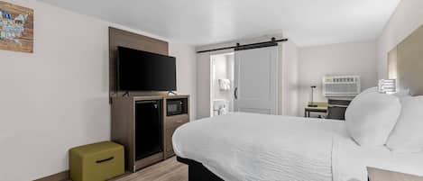 Habitación de hotel con cama, televisor, microondas, refrigerador pequeño, escritorio con lámpara y baño visible a través de una puerta abierta.