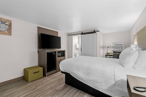 A hotel room with a bed, a television, a microwave, a small refrigerator, a desk with a lamp, and a bathroom visible through an open door.