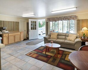 A living room with a sofa, coffee table, and a rug. There is a door leading outside, a window with a view, and a kitchen area with cabinets and a counter. - Econo Lodge Westminster, MA (Westminster)