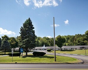 A road leading to a building with a sign for a motel. There are trees and a clear sky. - Econo Lodge Westminster, MA (Westminster)