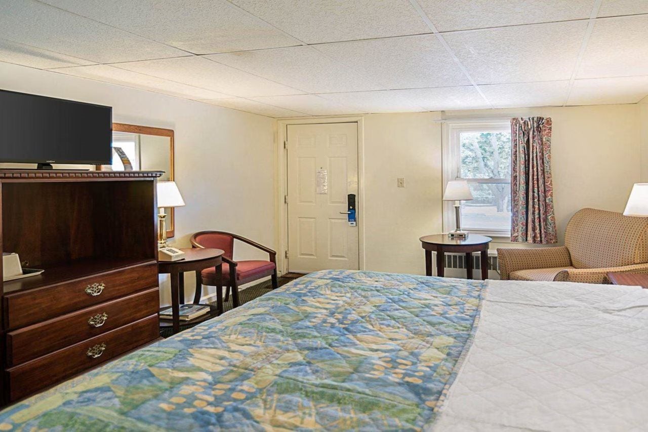 Una habitación de hotel con cama, escritorio, silla, televisor y puerta.