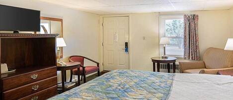 Una habitación de hotel con cama, escritorio, silla, televisor y puerta.