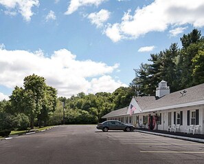 A motel with a car parked in front, surrounded by trees and a clear sky. - Econo Lodge Westminster, MA (Westminster)