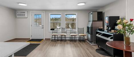 A compact kitchen with a dining area, a refrigerator, and a coffee machine.
