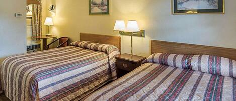 Habitación de hotel con dos camas, un escritorio, una silla, lámparas y dos cuadros en las paredes.