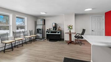 A modern kitchen with a coffee machine, a refrigerator, and a dining area with chairs and a table.