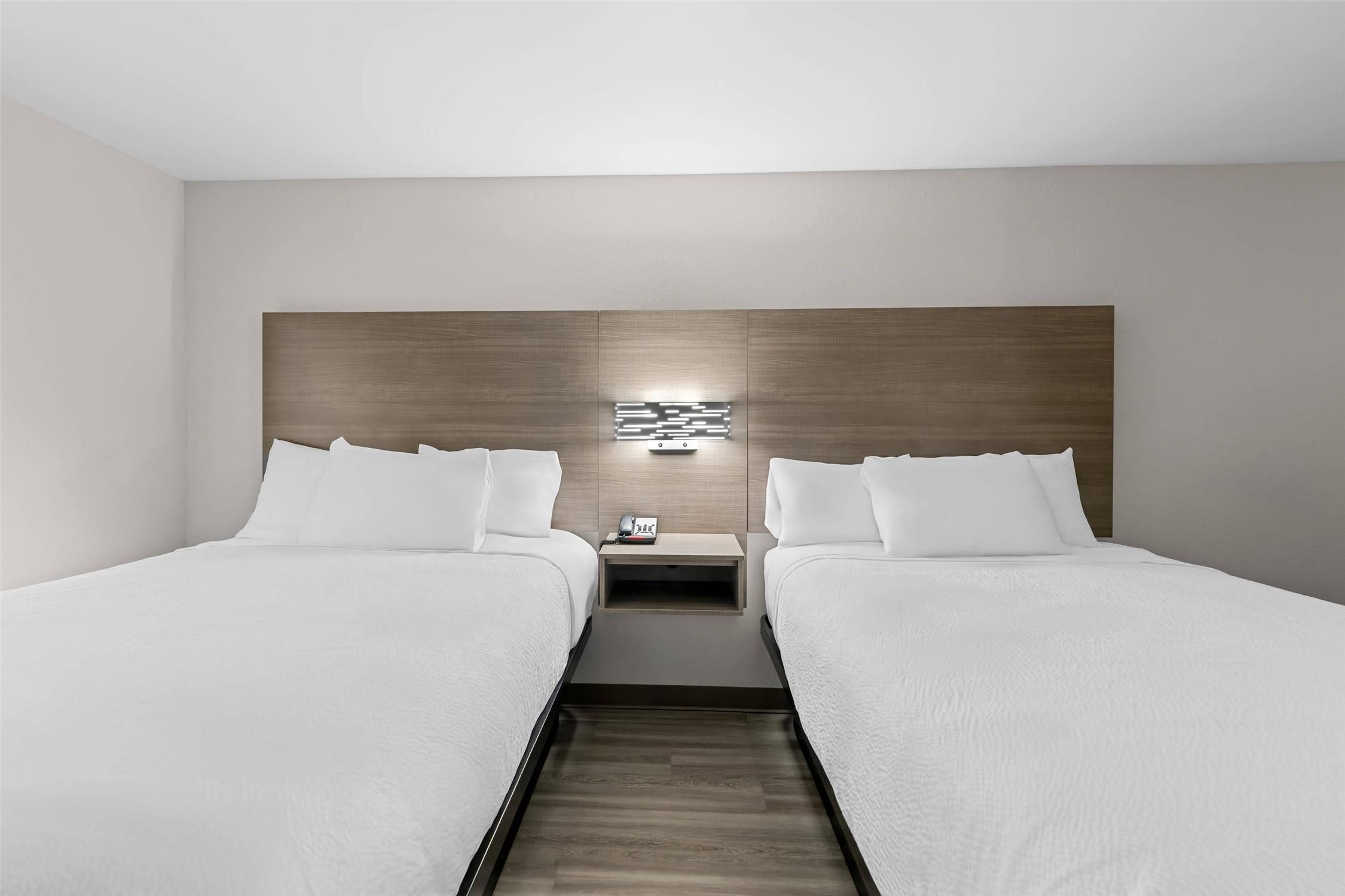 Une chambre d’hôtel avec deux lits, une table de chevet avec un téléphone et une lampe fixée au mur.