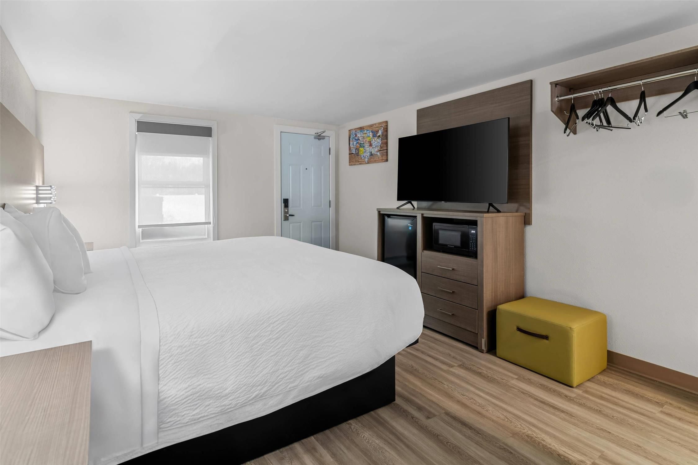 A modern hotel room with a large bed, a television, a wardrobe, and a small yellow storage unit.