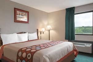 Una habitación de hotel con una cama, un cuadro en la pared, una ventana con cortinas y un aire acondicionado de pared.