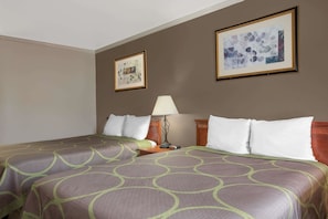 Une chambre d’hôtel avec un lit, une table de chevet, une lampe et deux tableaux encadrés au mur.