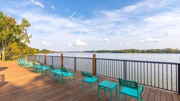 A wooden deck with turquoise chairs facing a lake.