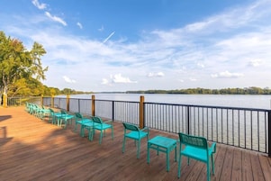 A wooden deck with turquoise chairs facing a lake.