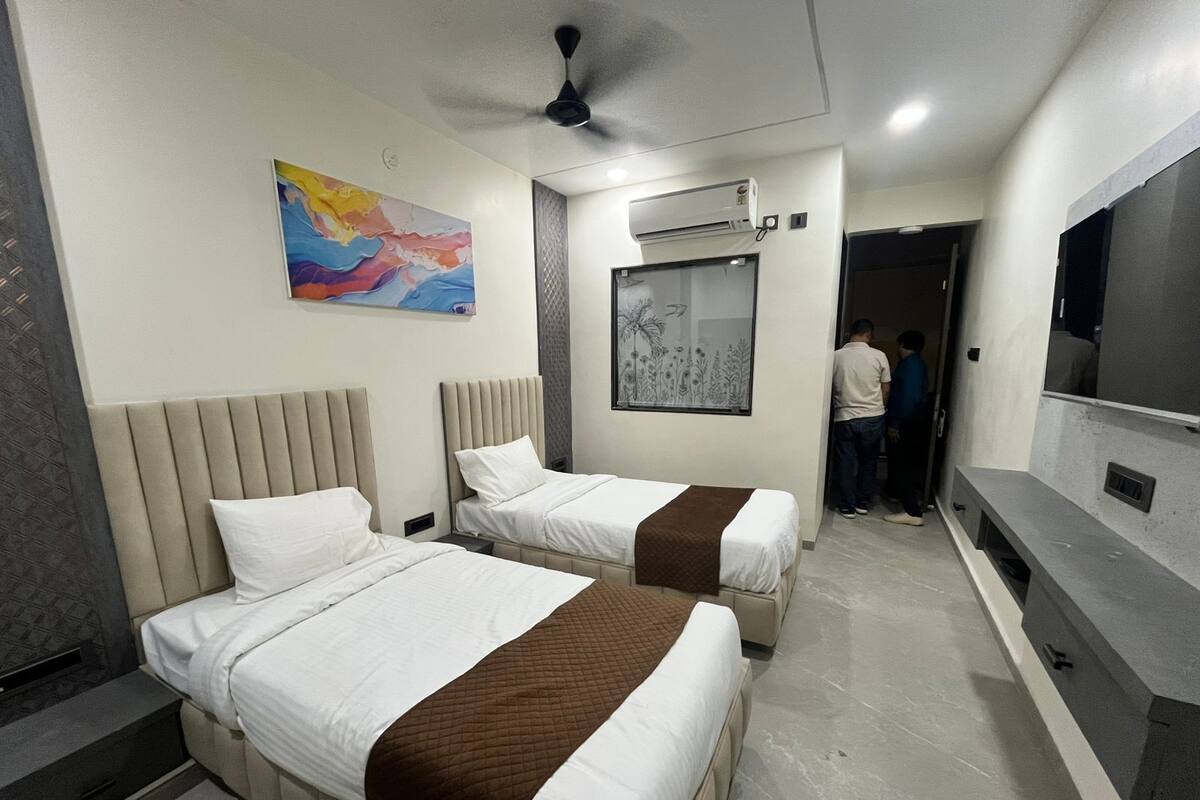 A hotel room with two beds, a ceiling fan, an air conditioning unit, a TV, and a painting on the wall.