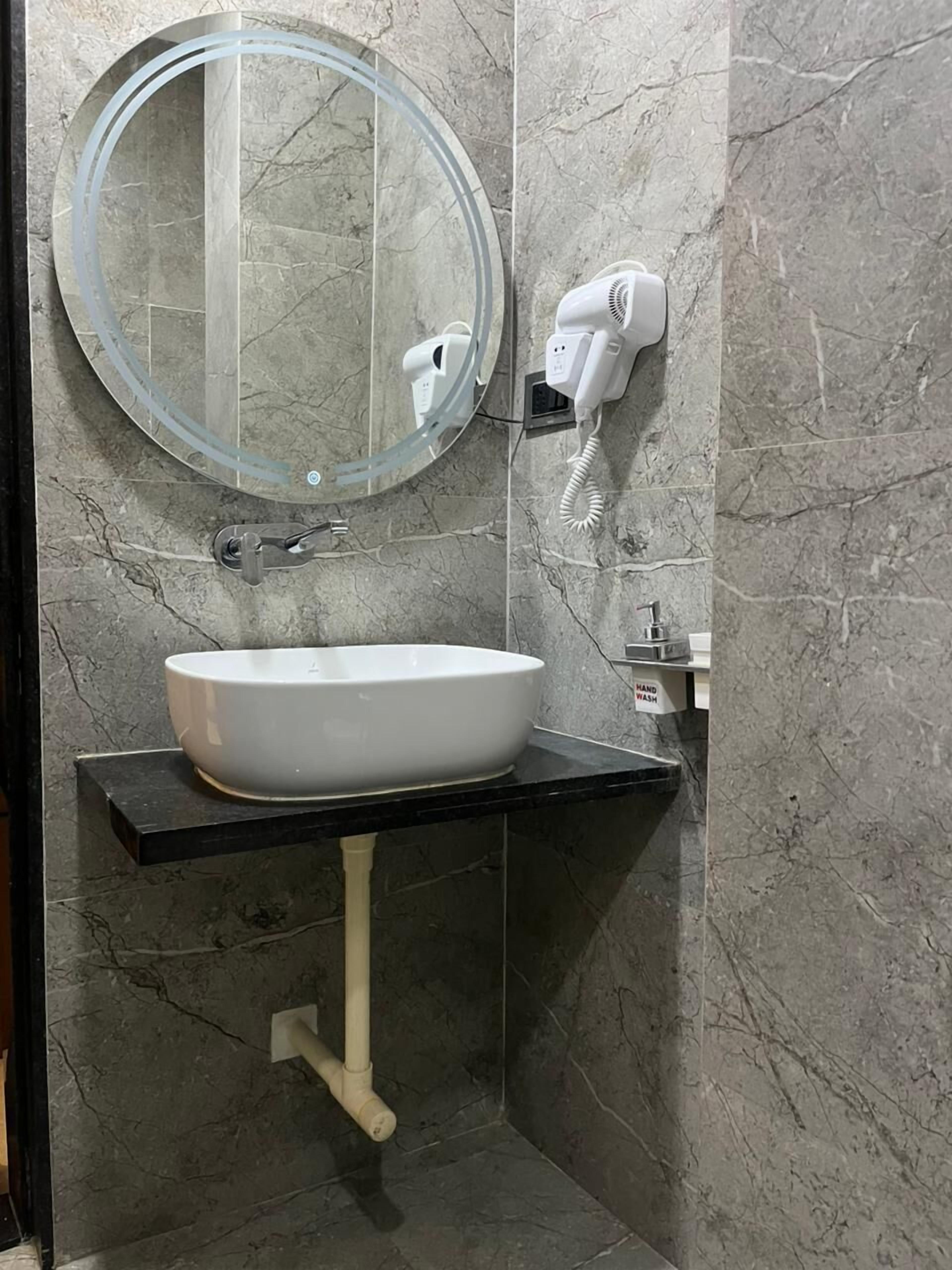A bathroom with a white sink, a round mirror, a hairdryer, and a hand wash station.