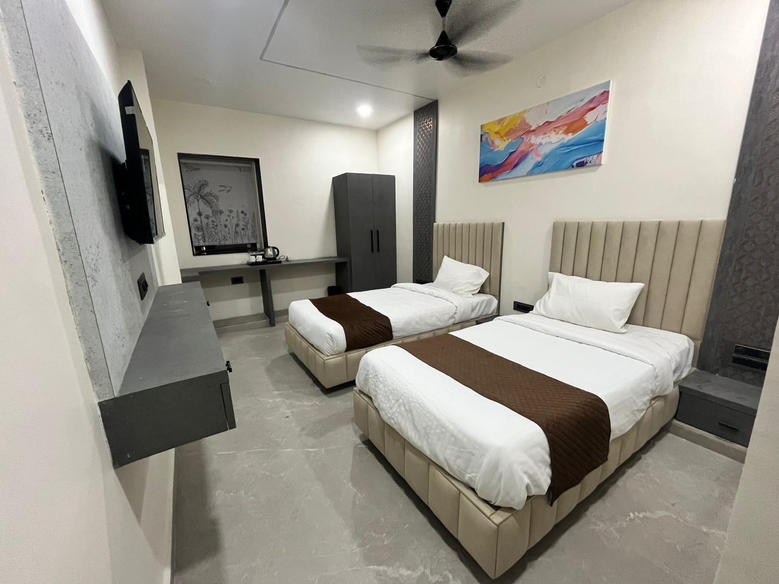 A hotel room with two beds, a desk, a TV, and a painting.