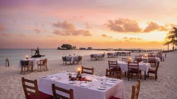A beachside dining area with tables set for two, overlooking the ocean at sunset.